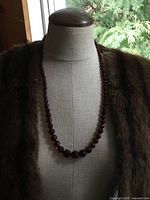 Necklace displayed on a mannequin wearing a brown fur garment, showing length and graduated bead sizes.