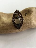 Front view showing marquise-shaped banded agate with surrounding garnet beads in sterling silver setting placed on a textured wooden display.