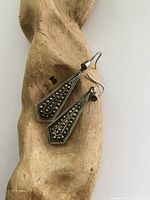 Photo showing pair of silver-tone dangle earrings with marcasite stones laid on a textured surface, length and design clearly visible.