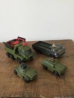 Top-front angle showing all four military toy trucks: missile launcher, troop carrier, armored car, and jeep with figurine.