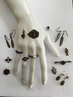 Display of full set on a white hand-form mount showing rings on fingers, earrings and pins arranged around