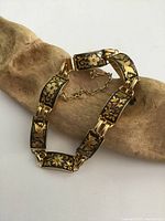 Photo of vintage Japanese floral panel bracelet shown on light wood display, showing gold floral designs and safety chain.