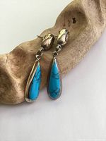 Pair of large Mexican sterling silver turquoise drop earrings with visible tarnish and surface wear, lying on a carved wooden display