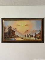 Full view of the oil painting showing the framed landscape with cabin, water, camels, and person.