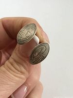 Two oval-shaped sterling silver stud earrings showing North West Coast Indigenous carved design held in hand to show size and detail.