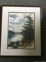 Framed watercolour painting showing a lake or river scene with pine trees and cloudy sky.