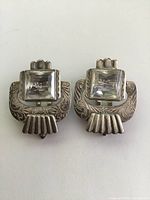 Front view of pair of Art Deco sterling silver shoe clips each with large top square-cut clear crystal and engraved floral pattern on clip body