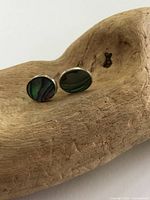 Front view of the pair of sterling silver stud earrings with oval-shaped iridescent abalone shell inlay, placed on wood surface.