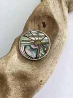 Front view of round pendant showing colorful abalone shell sun design inlay with silver outlines and border, placed on wood.
