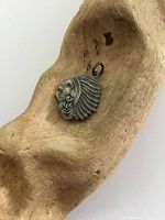 Silver charm with Native American head headdress resting in a wooden bowl, showing front detail.