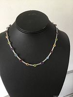 Necklace displayed on black bust showing multicolored gemstones and sterling silver chain with square-cut stones.