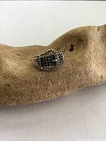 Sterling silver ring with black hematite buckle design resting on a textured natural wood surface.