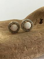Pair of gilt sterling silver stud earrings with round opal stones surrounded by clear stones displayed on textured wooden surface.