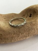 Top and angled front view of the sterling silver ring showing decorative square-shaped settings along the front band, placed on a wooden surface.