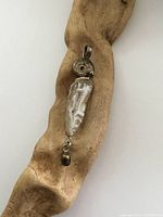 Front view of the pendant showing shell centerpiece, quartz detail at top and pearl drop at bottom on a wooden backdrop.