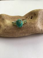 Top view of sterling silver ring with oval turquoise center stone and two rectangular peridot stones on each side, placed on a wooden display.