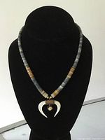 Front view of vintage beaded necklace displayed on black necklace stand, showing pattern of beads and central mother of pearl pendant shaped like horns with small round mother of pearl piece.