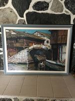 Framed oil painting depicting a traditional bridge and canal scene with boat and buildings.
