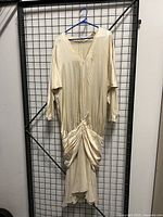 Front view of the 1920's silk dress hanging on a blue hanger against a grid wall.