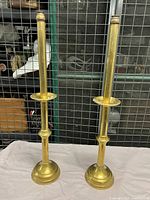 Pair of 22-inch tall brass church candlesticks standing upright showing both holding candle tubes and round weighted bases.