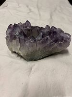 Side angle view of purple amethyst crystals on geode tea light holder, showing jagged pointed crystal formations and rough natural base.