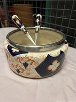 Decorative serving bowl with silver plate rim and intricate blue and orange floral and geometric patterning on cream background. Inside appears to be neutral tone.