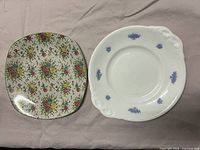 Two antique serving plates: one square floral plate and one round plate with blue floral details on white.