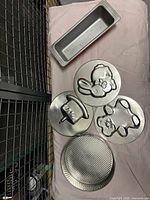 Overview of the bread pan and four springform pan bottom inserts showing teddy bear, birthday cake, bunny rabbit, and textured plain designs.