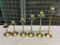 Front angle showing all 7 brass and copper graduated candle holders lined up by height from shortest to tallest