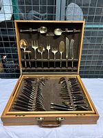 Full view of the open wooden case showing upper section holding serving utensils and knives, lower section holding forks and spoons with rosewood handles and brass heads.