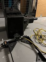 Dry ice machine unit and attached electrical cord with rolling base showing caster wheels, captured in industrial setting.