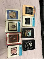 Top view of eight 8 track tapes showing front labels and cover art including Village People, Cher, Neil Diamond, Anne Murray, Olivia Newton John, and Star Wars tapes.