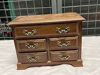 Front view of the wooden jewellery box showing six drawers with ornate metal handles.