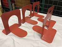 Five red metal bookends arranged side by side showing their upright supports with cutouts and flat bases.
