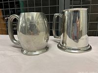 Two polished English pewter beer steins with glass bottoms shown side-by-side.