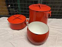Photo showing three red Dansk cookware items: two pots with lids and one enamel bowl, all with heavy use wear.