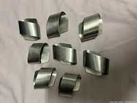 Top-down view of all eight pewter napkin rings arranged on a white surface, showing their twisted band design and uniform shape.