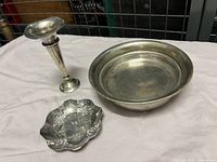 Silver plated false bottom dish, fluted bud vase and small tray displayed on white cloth background