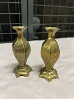 Pair of small solid brass bud vases with engraved patterns on sides, flared tops, hexagonal scalloped bases.