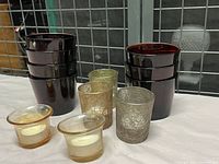 Various tea light holders of multiple colors and materials arranged on a wire mesh background, showing the different types included.