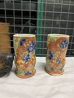 Two earthenware cups with colorful floral designs shown side-by-side on a surface.