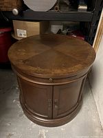 Round wooden side table with inlaid wood pattern on top, showing scratches and wear.