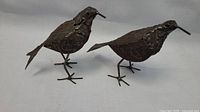 Two metal bird sculptures together on white background showing size difference and rustic hammered style