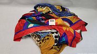Photo of eight colorful large light scarves piled together, showing various bright patterns including red, blue, yellow, purple, and black colors.