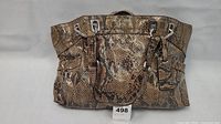 Front view of a large Makowsky purse showcasing snakeskin patterned leather with front pockets, dual handles, and metal hardware.