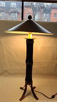 Full view of the lit lamp showing the faux bamboo style base with black finish and conical shade near window background