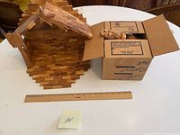 Wooden nativity stable and box containing nativity figures on a round table with a ruler added for scale.