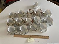 Photo showing 15 teacups with matching saucers in various floral patterns on a round white table with a ruler for scale.