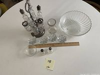 Full lot on white table showing bottle holder with six bottles, large ribbed glass bowl, smaller glass bowl, goblet, six votive candle holders, and salt and pepper shakers next to a wooden ruler for scale.