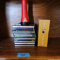 Photo showing the red flashlight atop a stack of music CDs and Canon PowerShot A2200 box standing upright on wood surface.